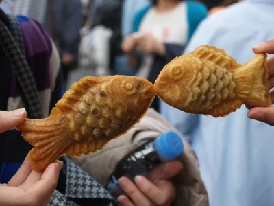 To personer holder opp taiyaki-kaker, som om fiskene kysser