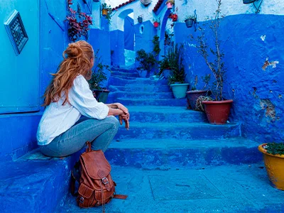 Kvinne sittende på trappen i den blå byen Chefchaouen, Marokko
