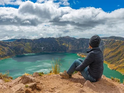 En kvinne sitter på kanten av kratersjøen Quilotoa i Ecuador.