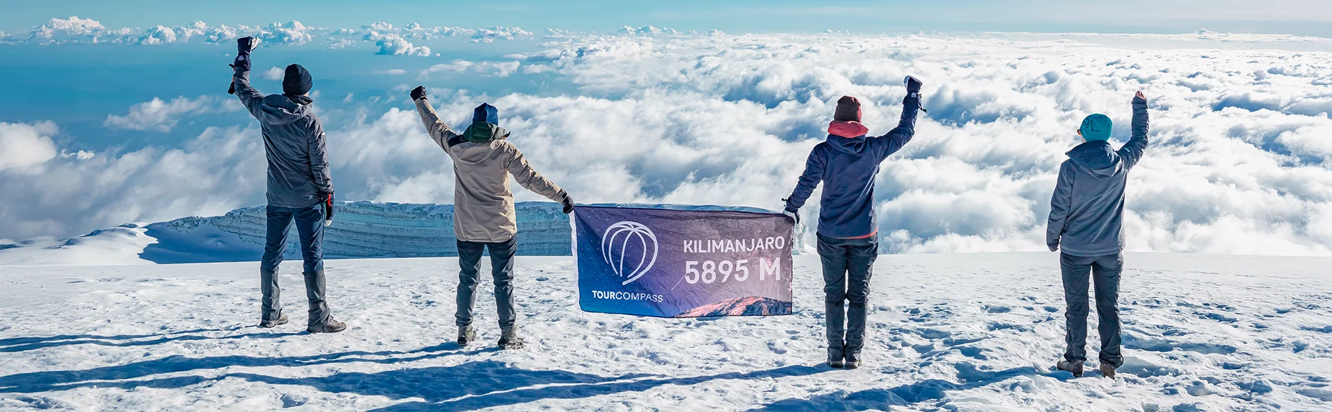 Gruppe står med TourCompass-banner på toppen av Kilimanjaro