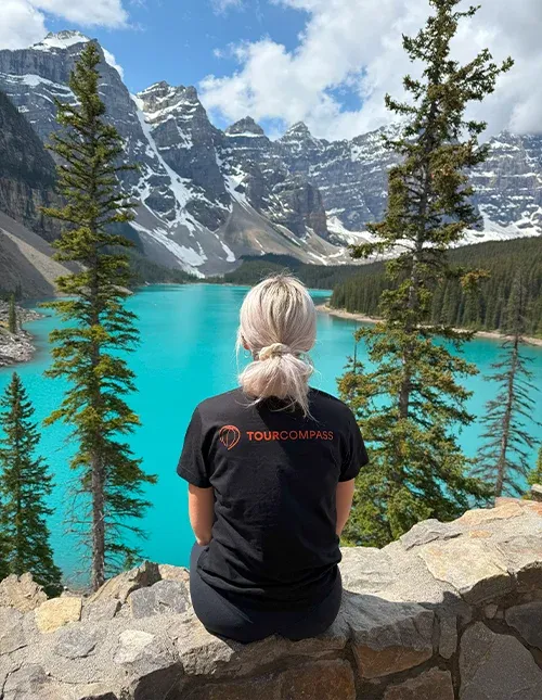 Kvinne med TourCompass T-skjorte ser utover en turkisblå innsjø og snøkledde fjell i Canada
